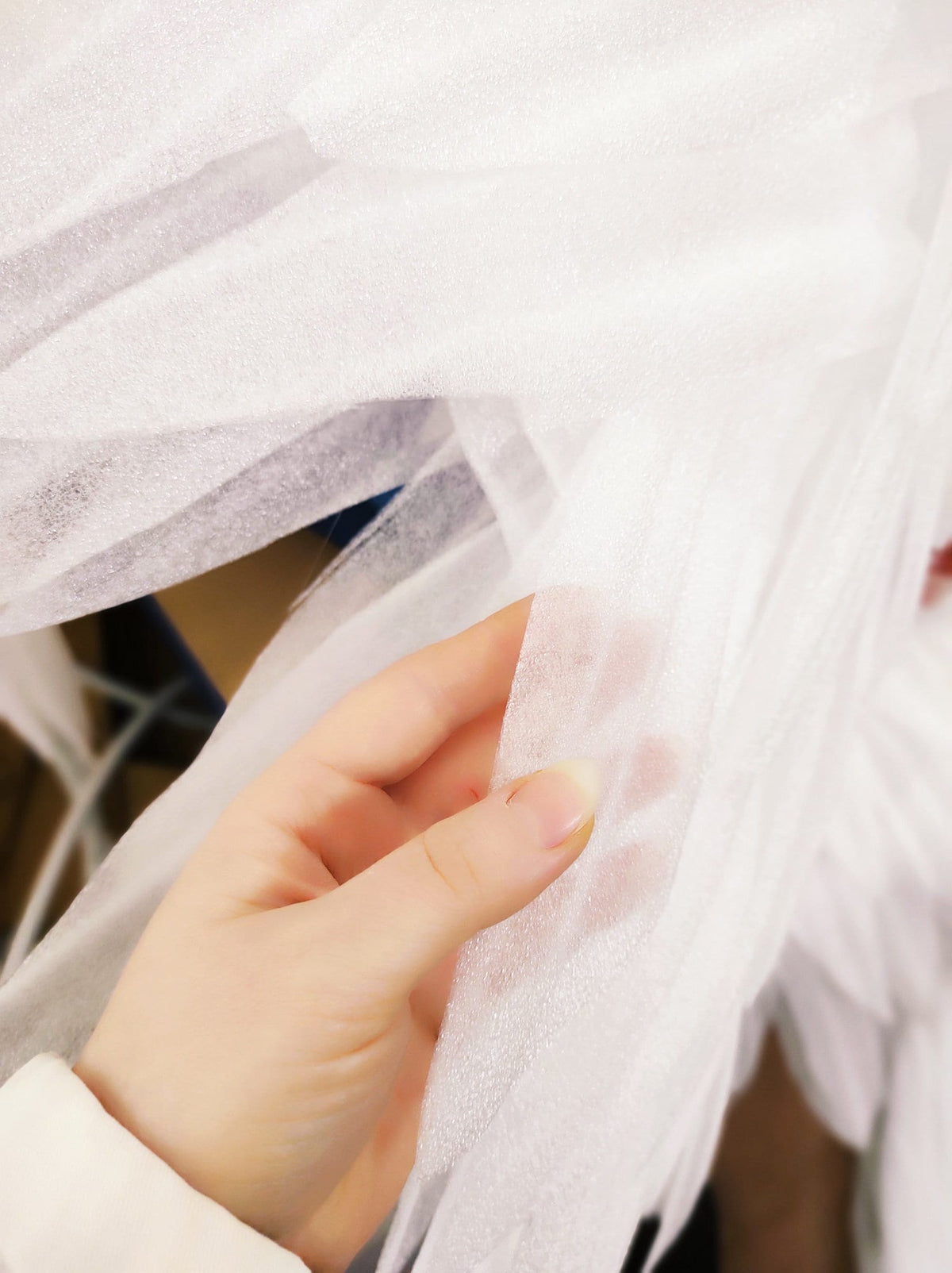 May include: A close-up of a white, sheer fabric with a textured surface. The fabric is being held by a hand.