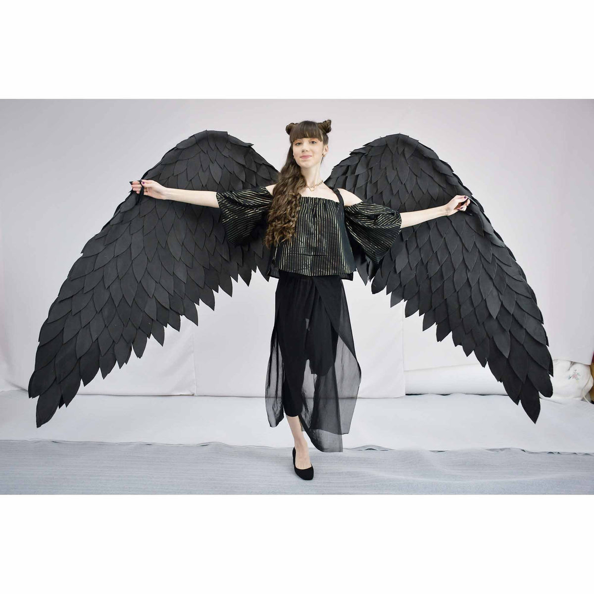 May include: A person wearing a black top and skirt with large black feathered angel wings.