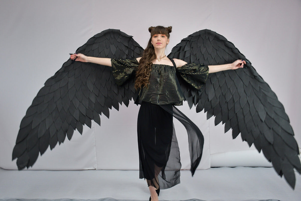 May include: A person wearing a black and gold striped top and black skirt with large black feathered wings.