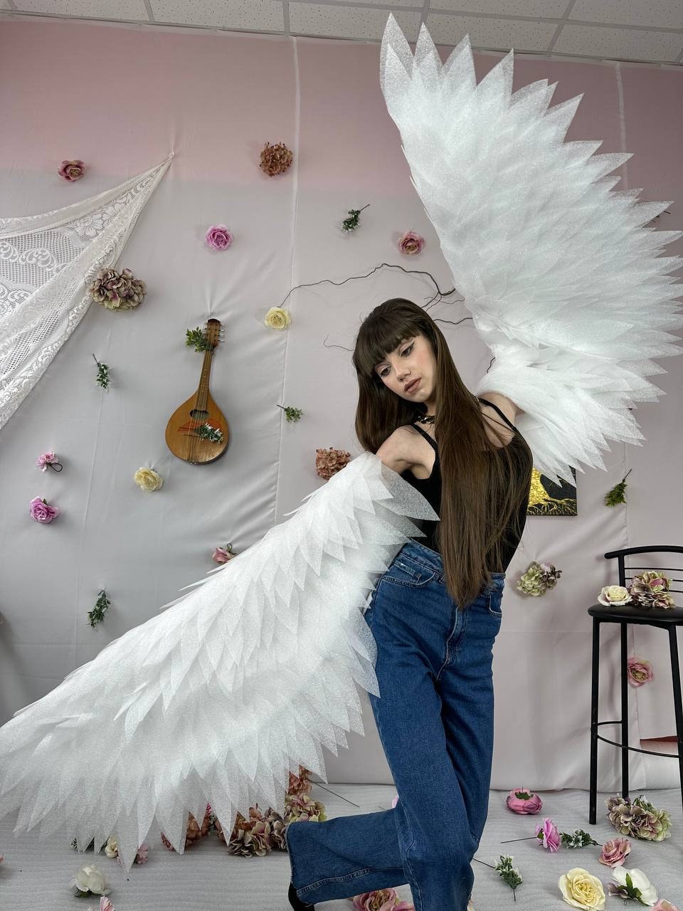 May include: A person wearing a black top and blue jeans with large white feathered angel wings.