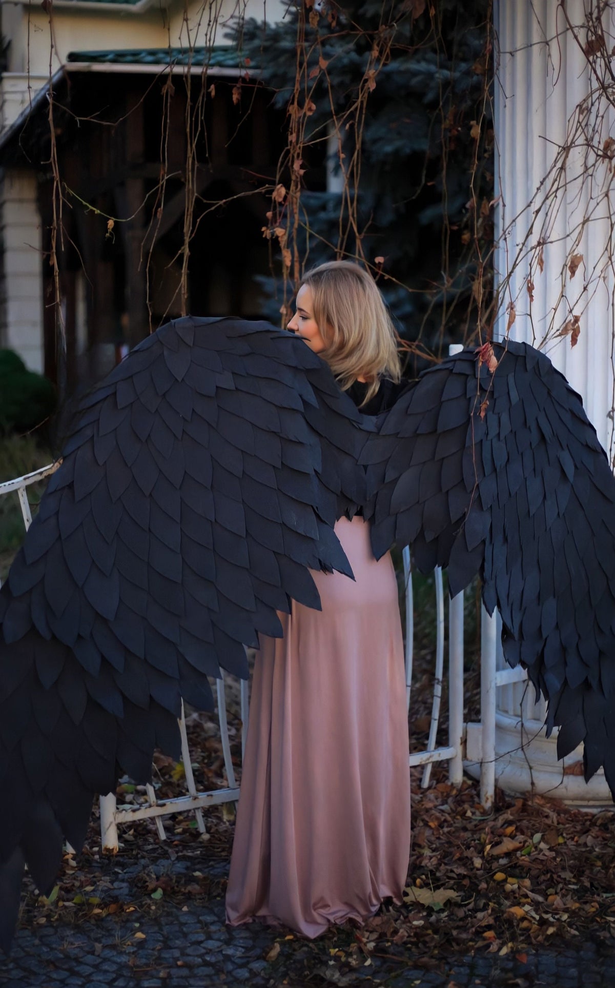 May include: A person wearing a long pink skirt and large black angel wings made of feathers. The wings are behind the person and are spread out.