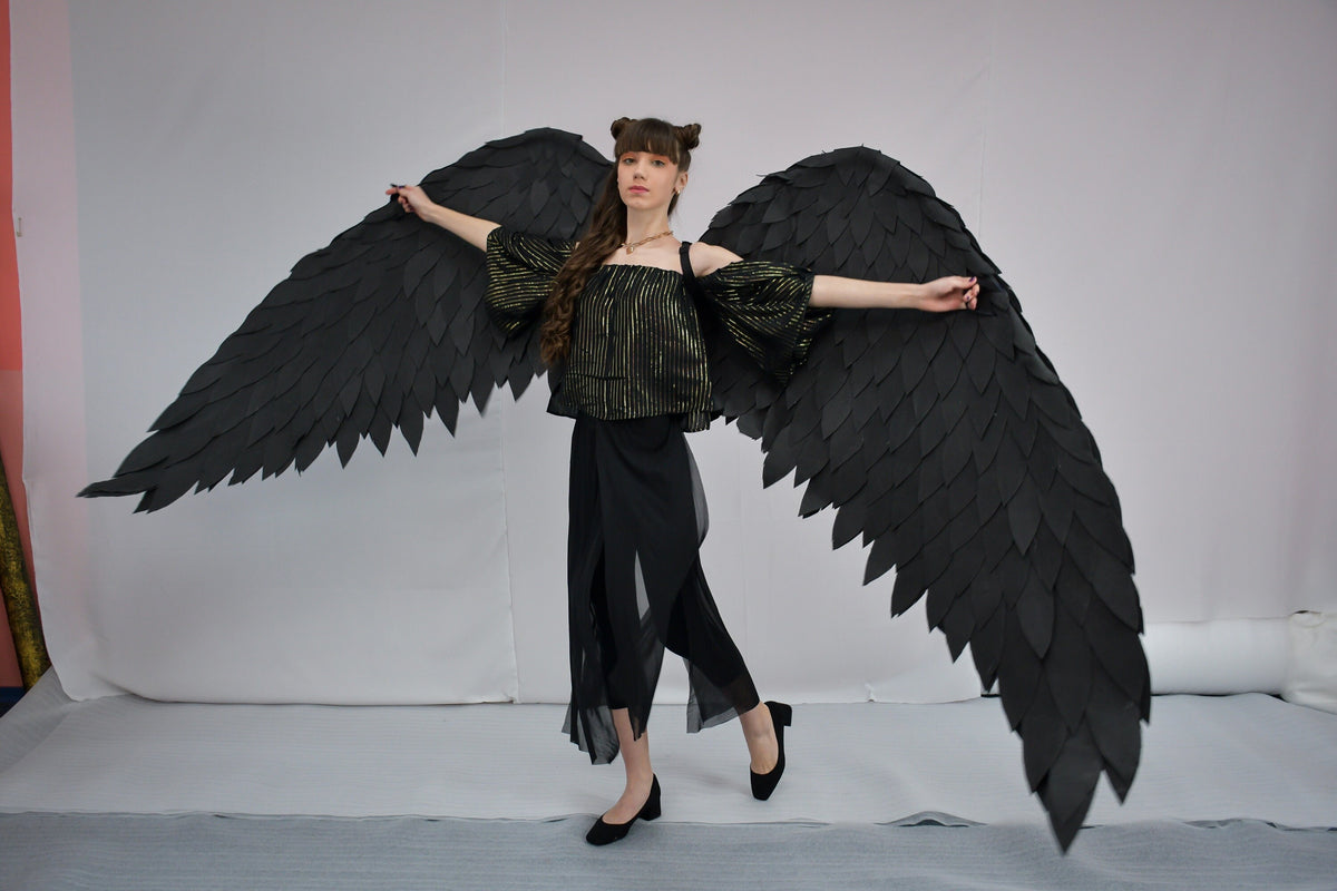 May include: A person wearing a black and gold striped top and black pants with large black feathered wings.