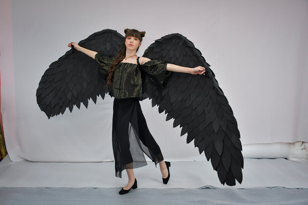 May include: A person wearing a black and gold striped top and black skirt with large black angel wings.
