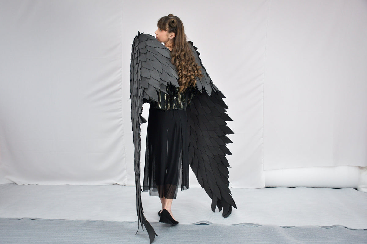 May include: A person wearing a black dress and large black feathered wings. The wings are made of many individual feathers and are very detailed.