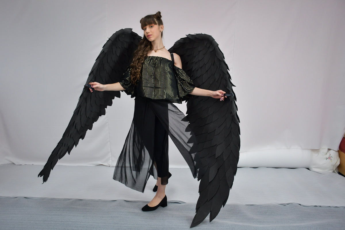 May include: A person wearing a black outfit with large black feathered wings. The wings are spread out behind the person.