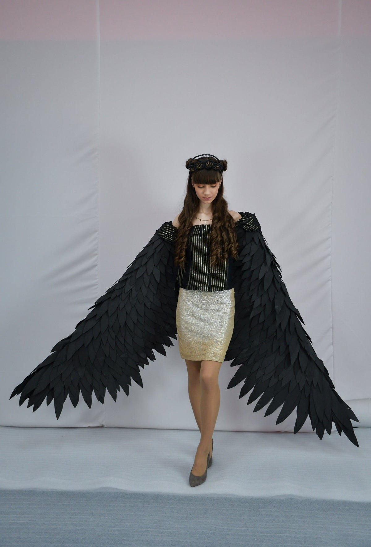 May include: A woman wearing a black and gold striped top and a gold skirt with black wings. She is wearing a black headband with gold accents.