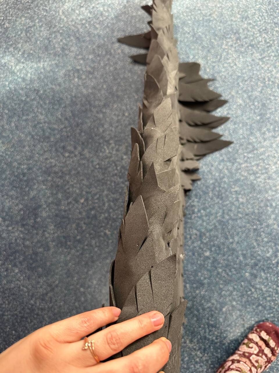 May include: A black foam dragon tail with a scaly texture. The tail is made up of many individual scales that are attached together.