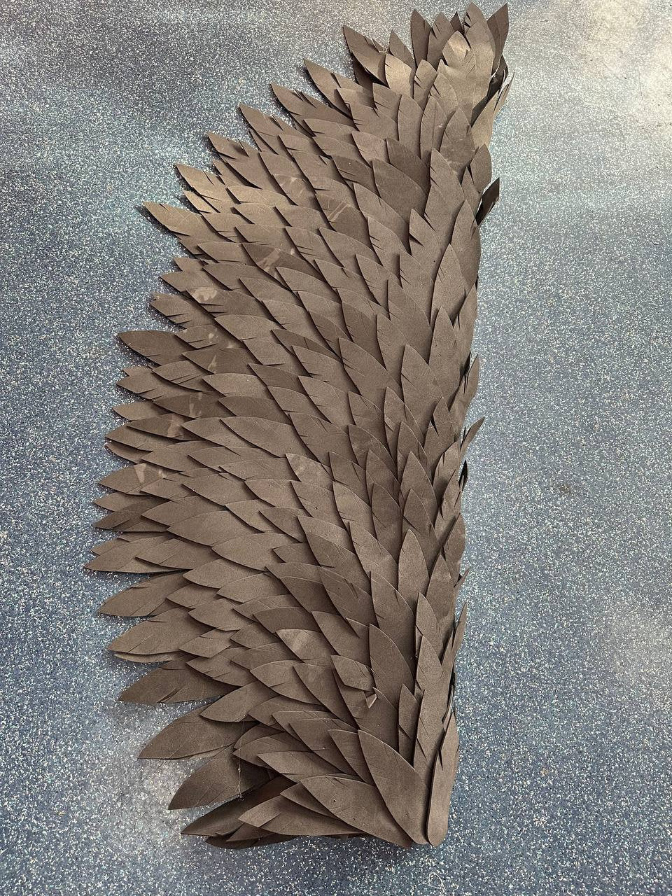 May include: A large, black, paper wing made of many individual feathers. The feathers are arranged in a fan shape, with the largest feathers at the bottom and the smallest feathers at the top.
