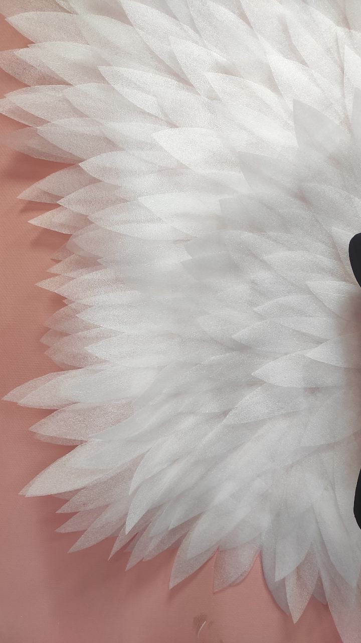 May include: Close-up of a white, layered, petal-like design against a soft pink background. The petals are translucent and arranged in a circular pattern, creating a delicate, textured effect. The design has a soft, ethereal quality.