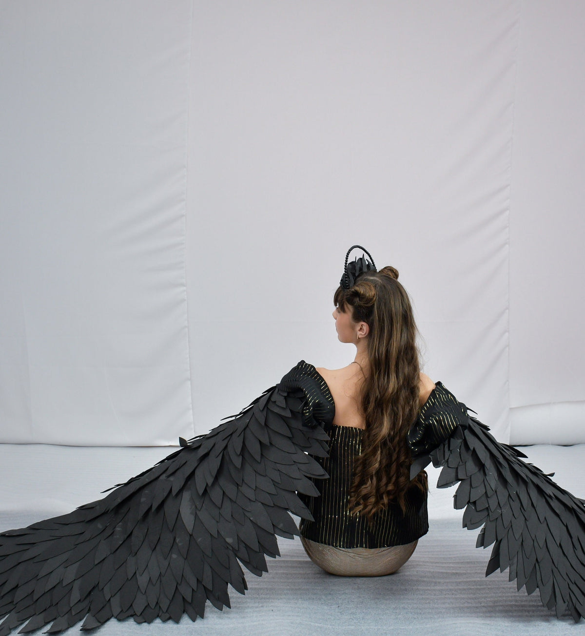 May include: A person wearing a black and gold top with large black wings made of feathers. The wings are spread out behind the person.