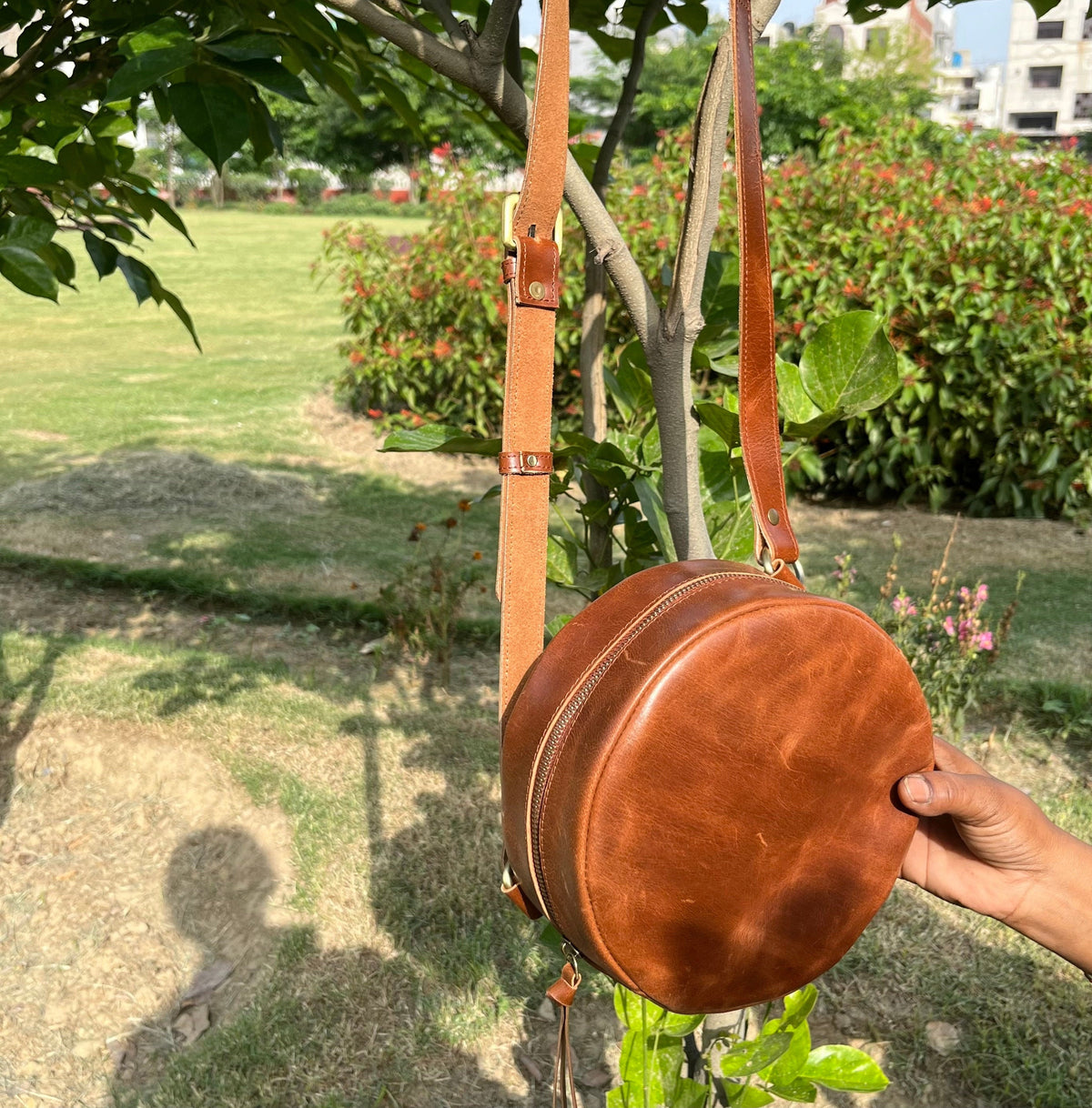 May include: A brown leather round crossbody bag with a long adjustable strap. The bag has a zipper closure and a small tassel.