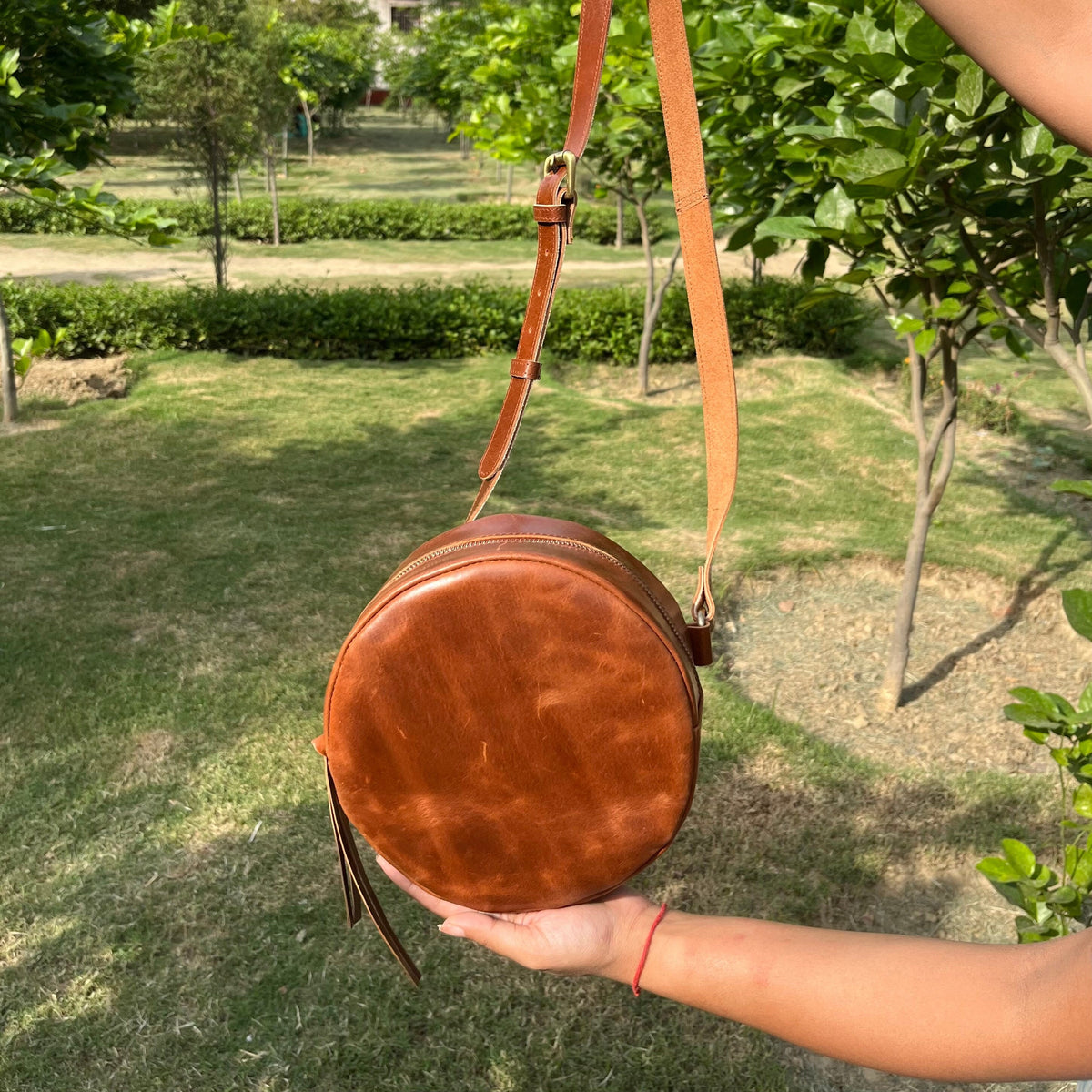 May include: A brown leather round crossbody bag with a long strap. The bag has a flap closure and a tassel.