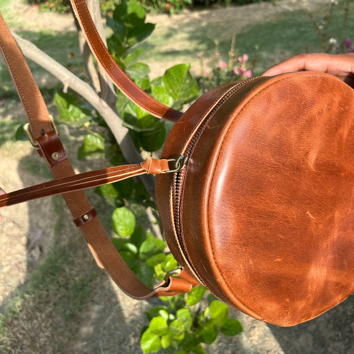 May include: A brown leather round crossbody bag with a zipper closure and a long adjustable strap.