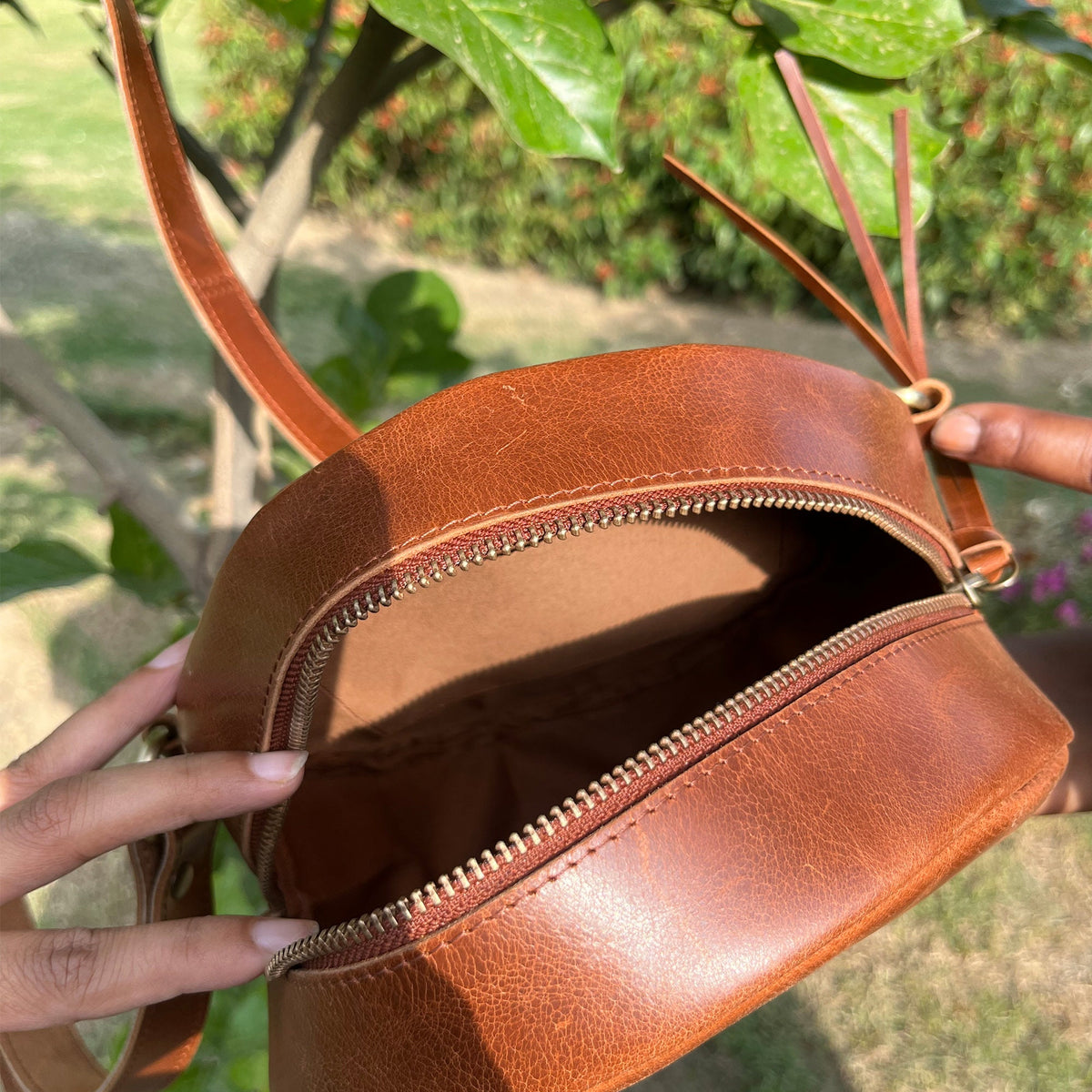 May include: A brown leather round crossbody bag with a zipper closure. The bag is open and the inside is visible.