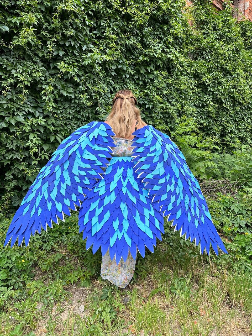 May include: A pair of large, blue and turquoise wings made of layered felt. The wings are shaped like bird wings and have a feathered texture.