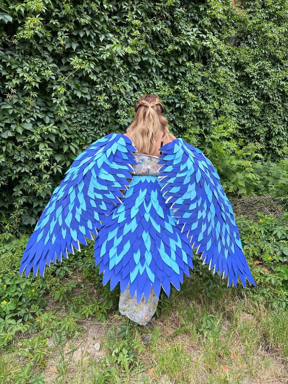 May include: A pair of large, blue and teal angel wings made of felt. The wings are layered and have a scaly texture.