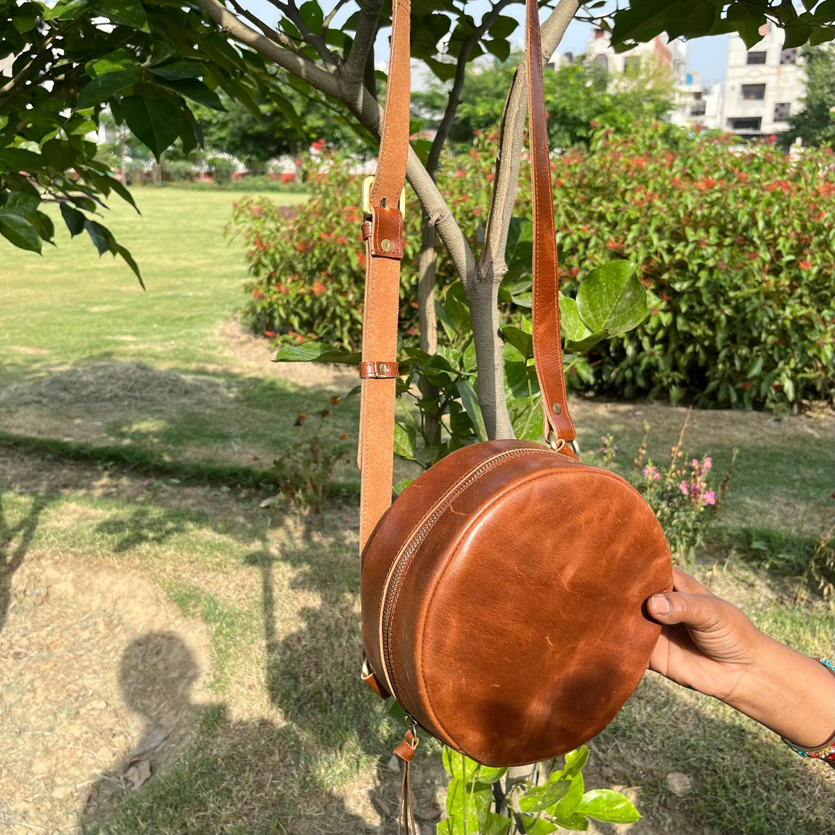 May include: A brown leather round crossbody bag with a long adjustable strap. The bag has a zipper closure and a flap.