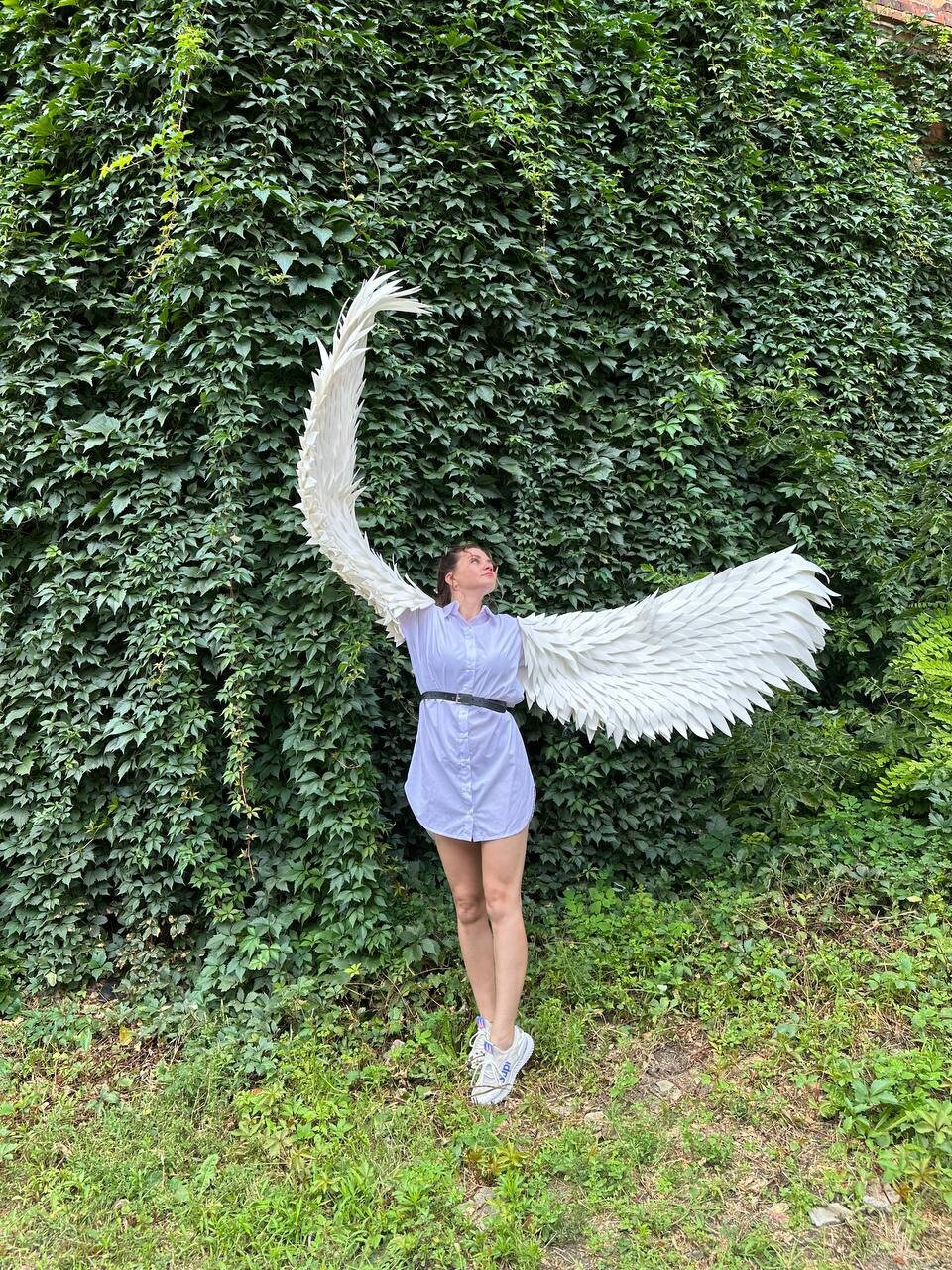 May include: A person wearing a white shirt and jeans with a pair of large white angel wings. The wings are made of feathers and are spread out behind the person.