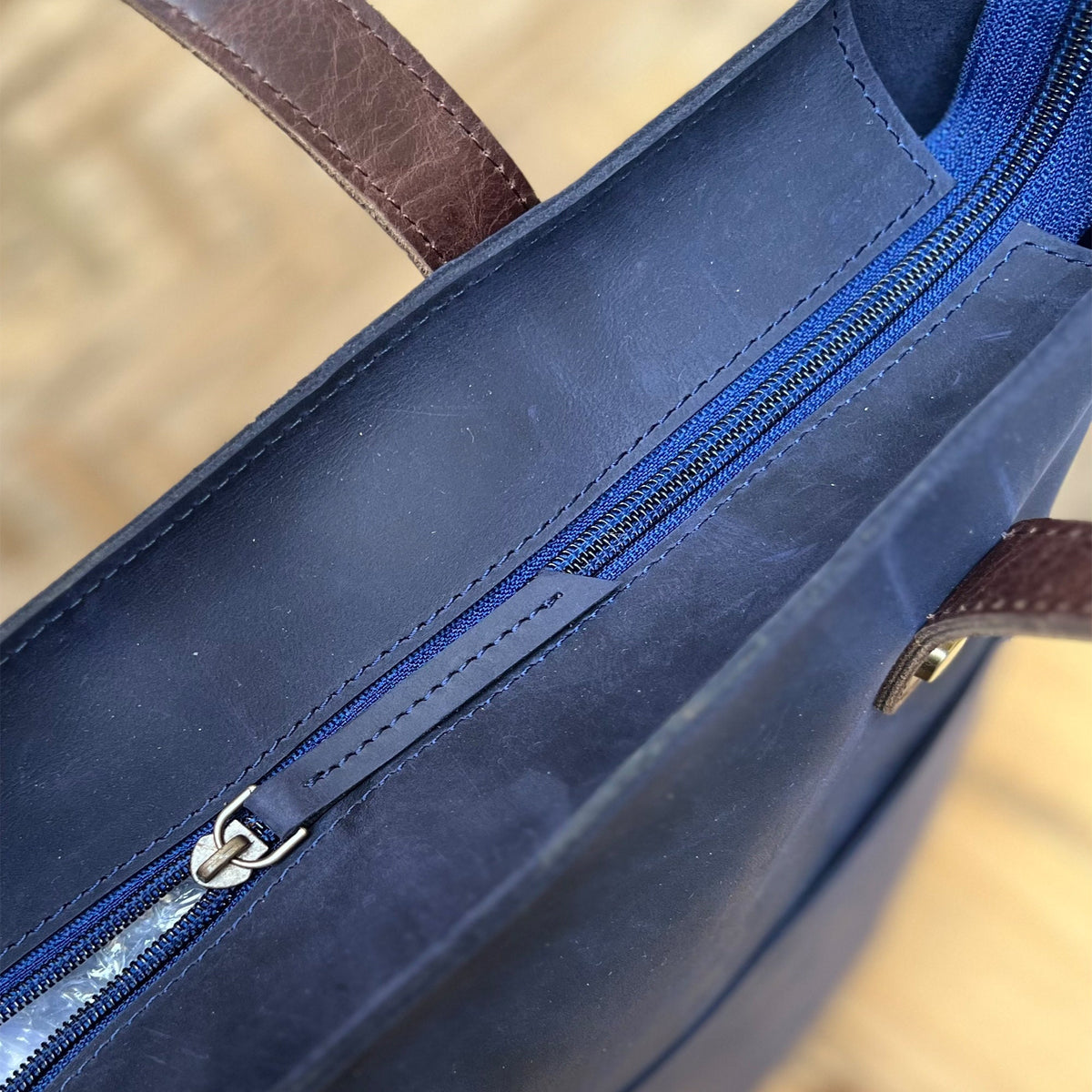 May include: A navy blue leather tote bag with a brown leather handle and a zipper closure.