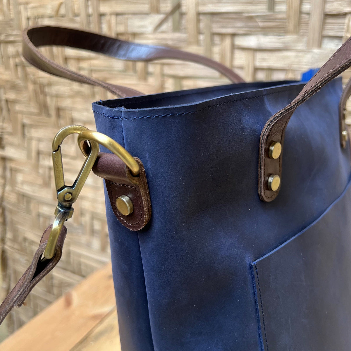 May include: A navy blue leather tote bag with brown leather straps and gold hardware. The bag has a front pocket and a top zipper closure.