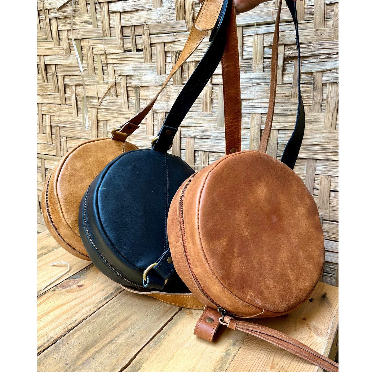 May include: Three round leather crossbody bags in brown, black, and tan. The bags have a zipper closure and a long adjustable strap.