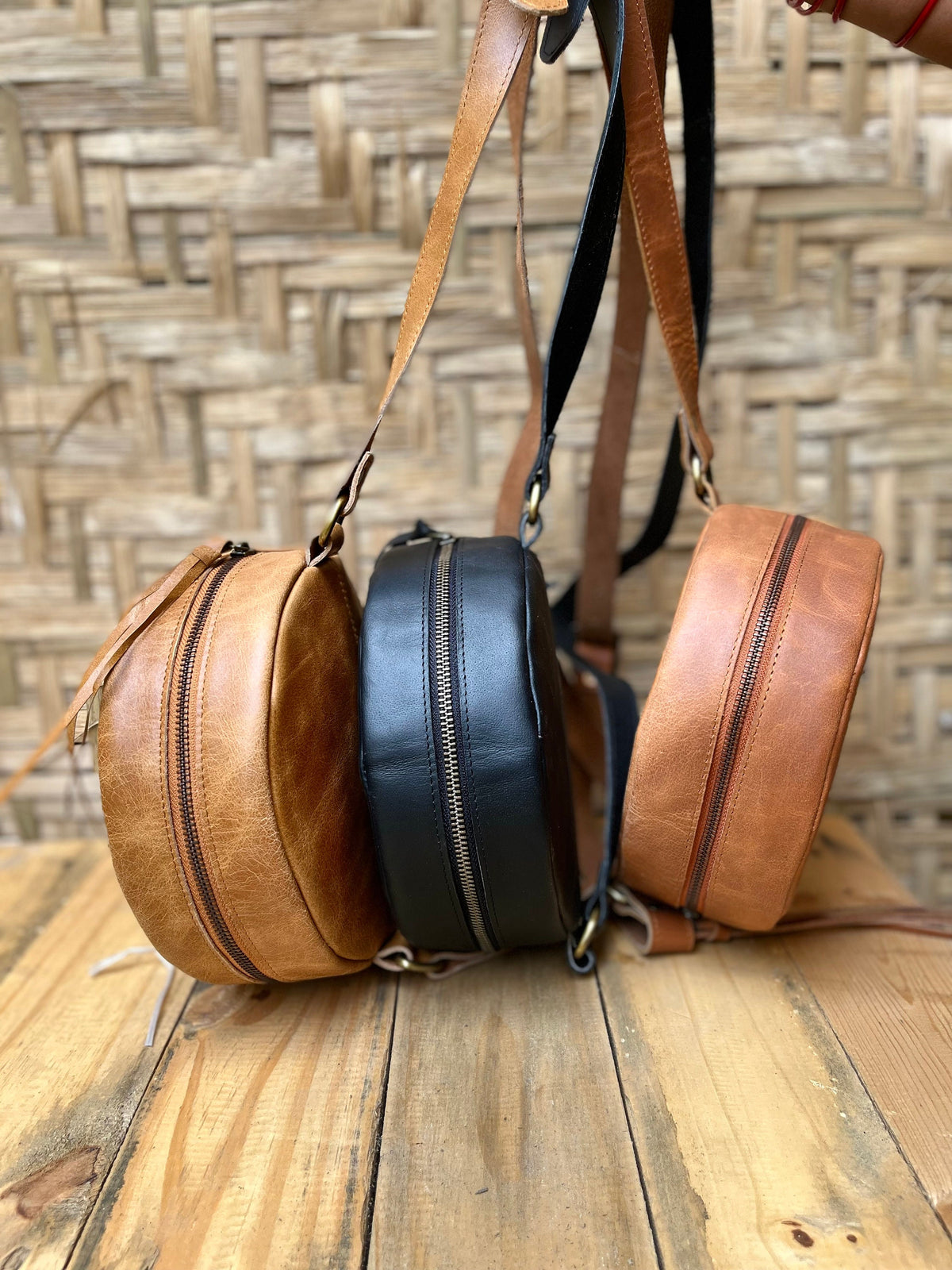 May include: Three round leather crossbody bags with adjustable straps. The bags are brown, black, and tan.