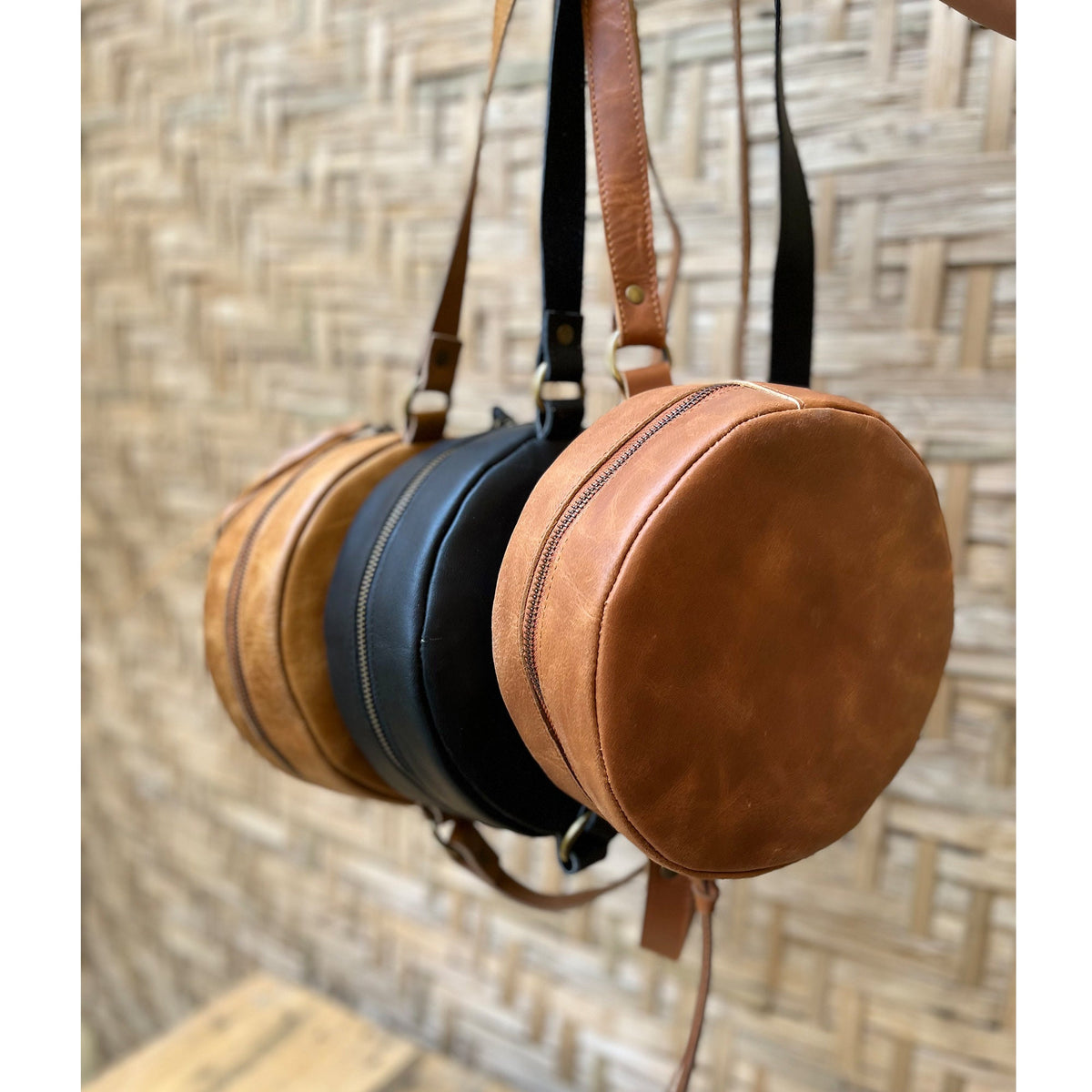 May include: Three round leather bags with adjustable straps. The bags are brown, black, and tan.