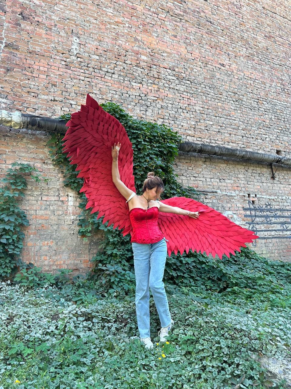 May include: A person wearing a red corset and blue jeans with large red feathered wings.