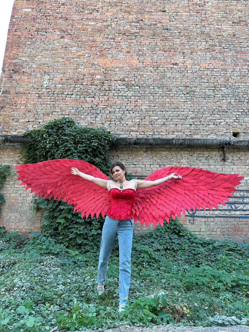 May include: A person wearing a red corset and blue jeans with large red feathered wings spread out behind them.