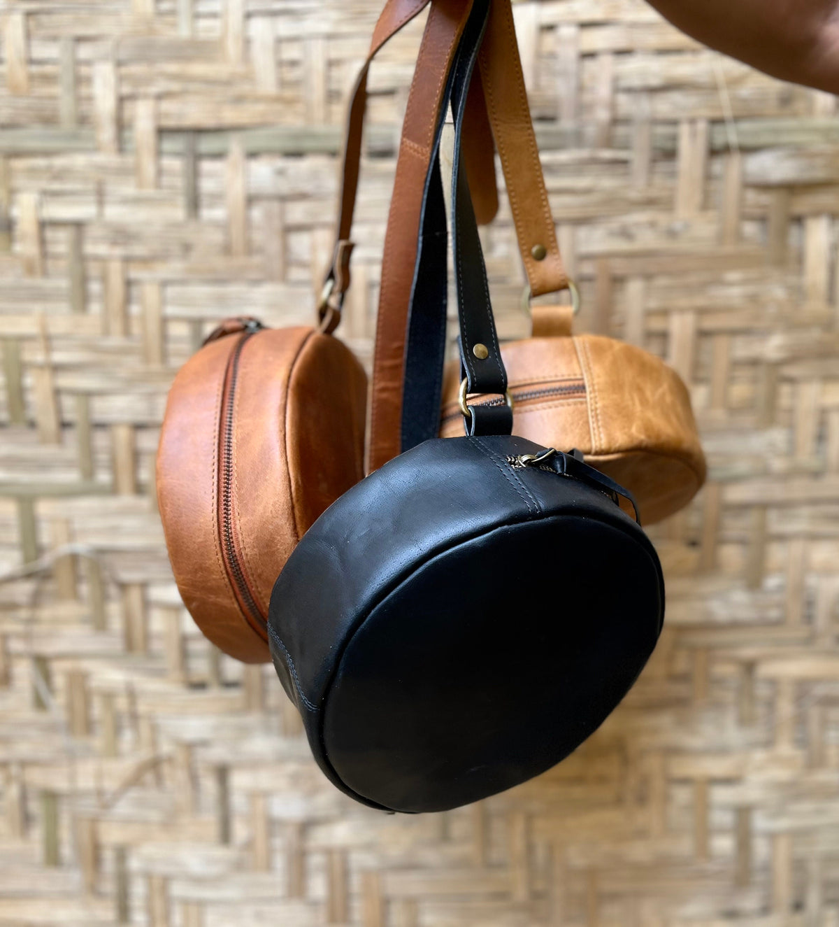 May include: Three round leather bags with adjustable straps. Two are brown and one is black.