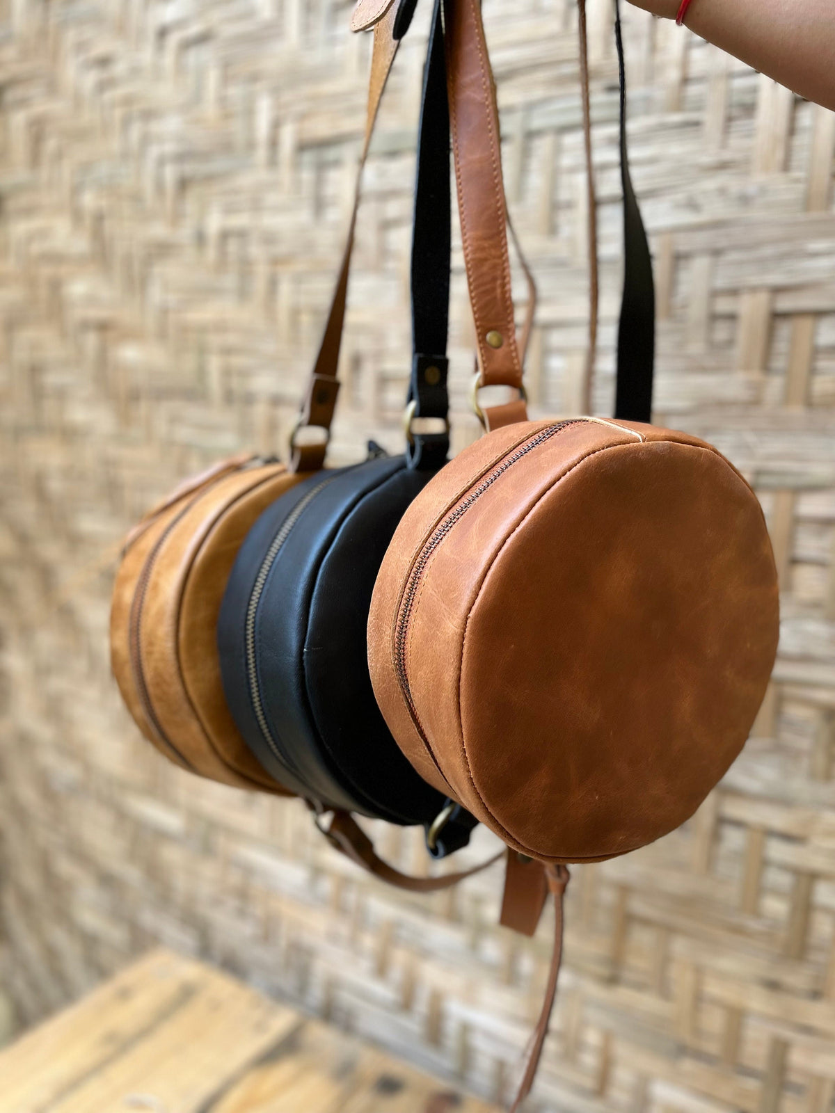 May include: Three round leather bags hanging from their straps. The bags are brown, black, and tan.