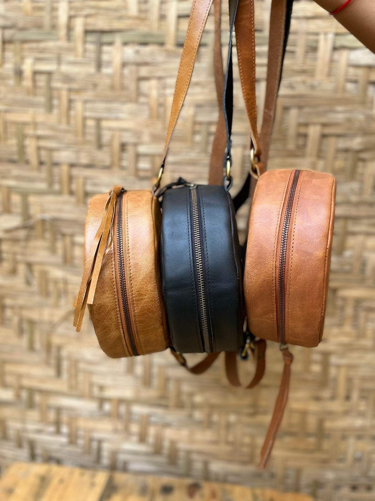 May include: Three round leather bags with adjustable straps. The bags are brown, black, and tan.