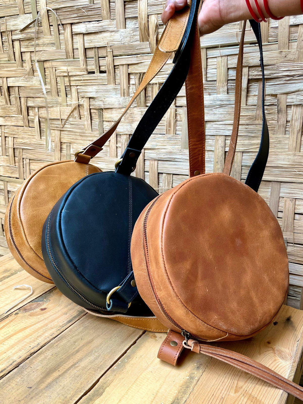 May include: Three round leather handbags in brown, black, and tan. Each bag has a long strap and a zipper closure.