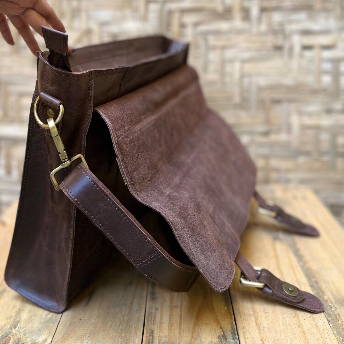 May include: A brown leather messenger bag with a flap closure and a long adjustable strap. The bag has a brass buckle and a brass clasp.