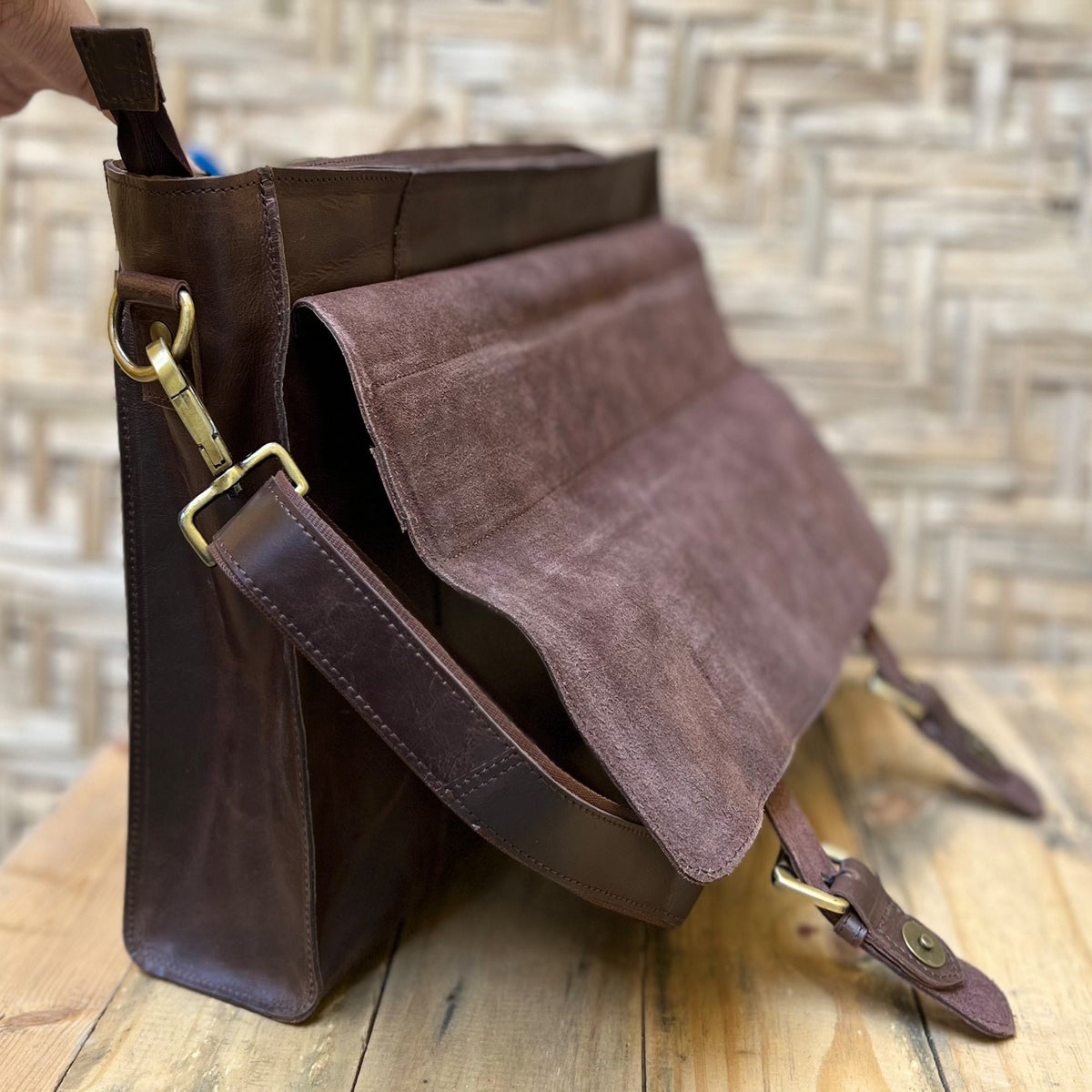 May include: A brown leather messenger bag with a flap closure and a long adjustable strap. The bag has a suede-like lining and brass hardware.
