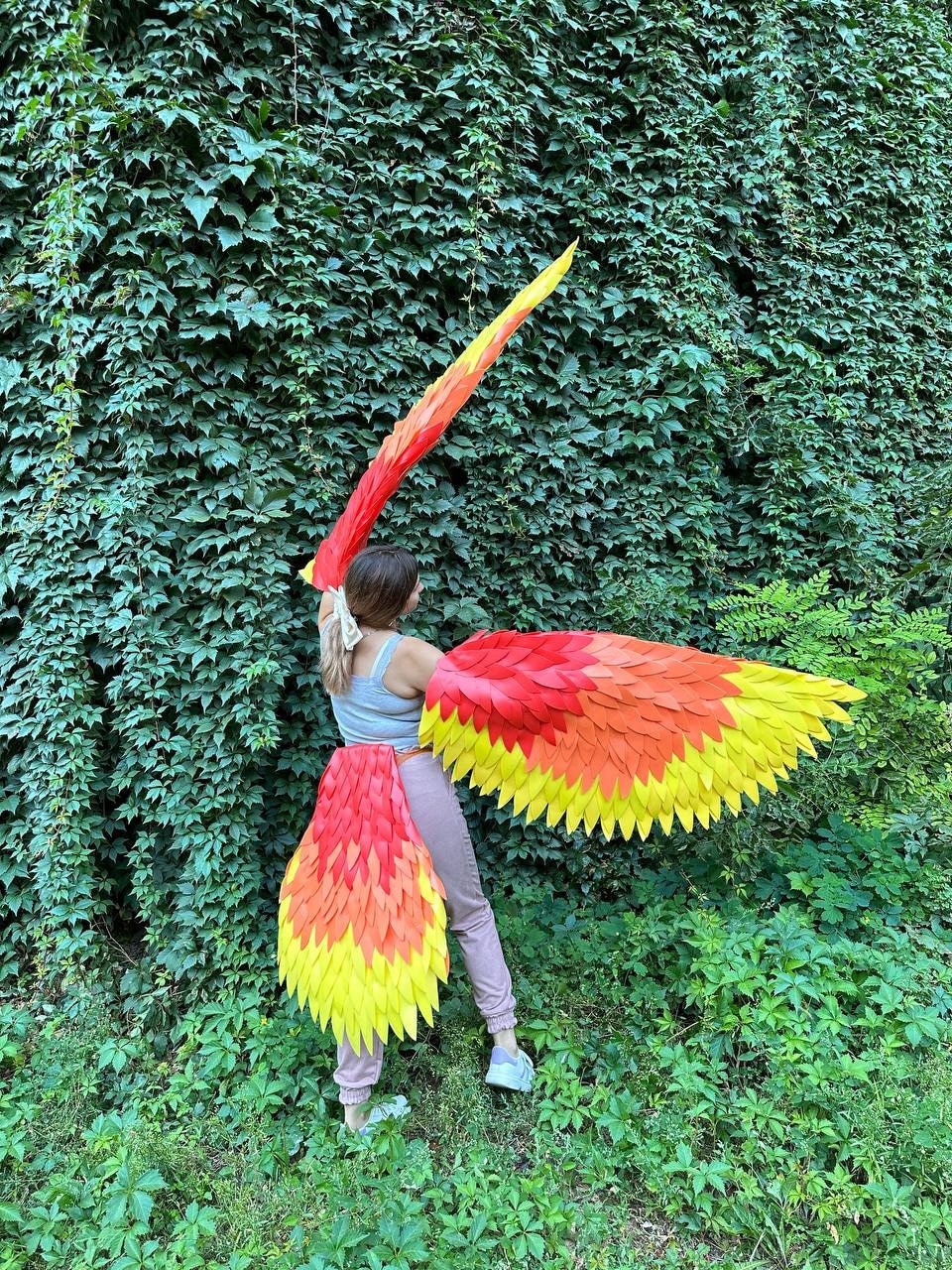 May include: A vibrant, handmade phoenix costume with large, layered wings and a tail. The wings and tail feature a gradient of colors, transitioning from red to orange and yellow. The costume is designed to be worn, suggesting a cosplay or theatrical theme.