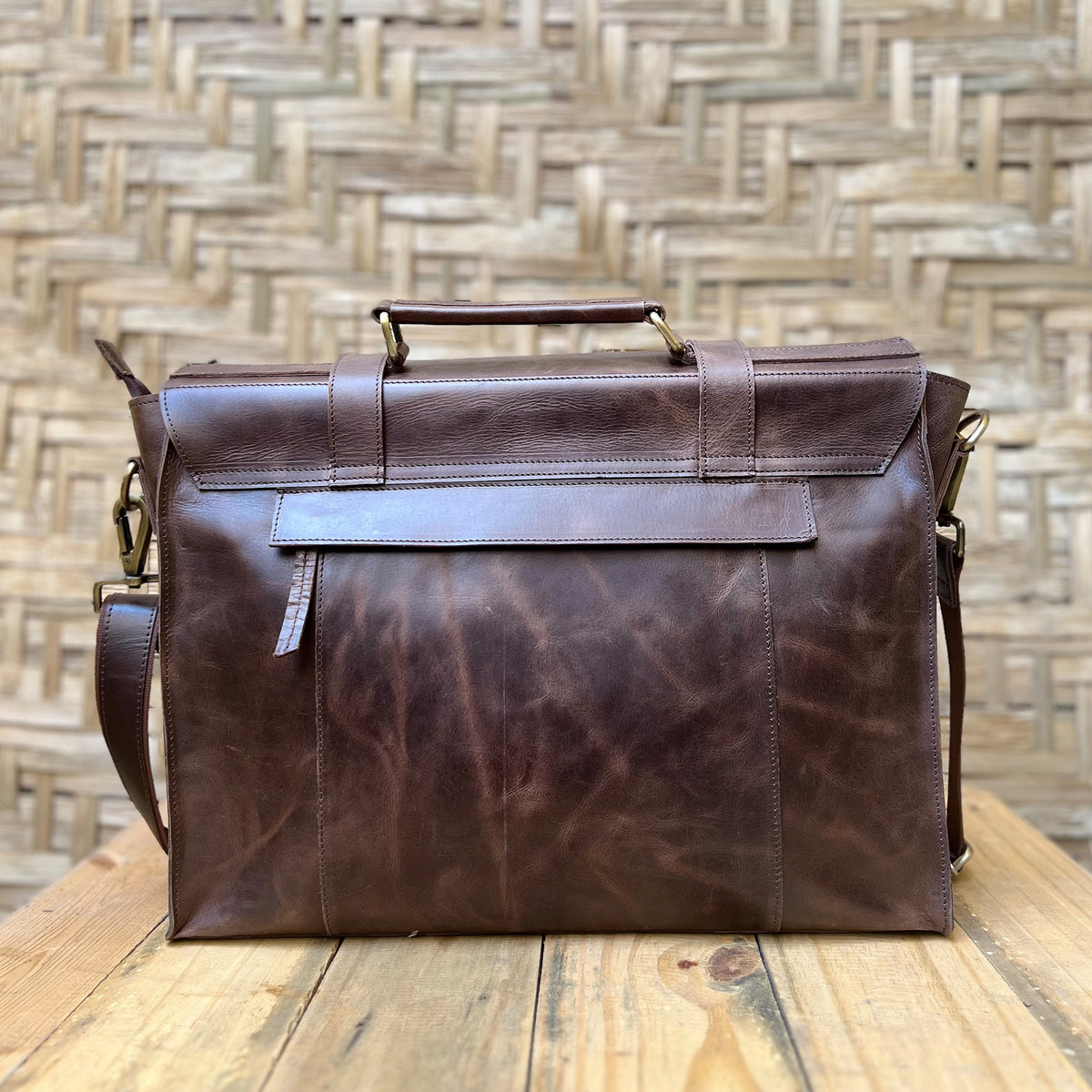 May include: A brown leather briefcase with a top handle and a shoulder strap. The bag has a flap closure and a front pocket.