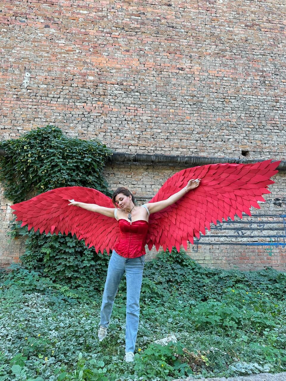 May include: A person wearing a red corset and blue jeans with large red feathered angel wings.