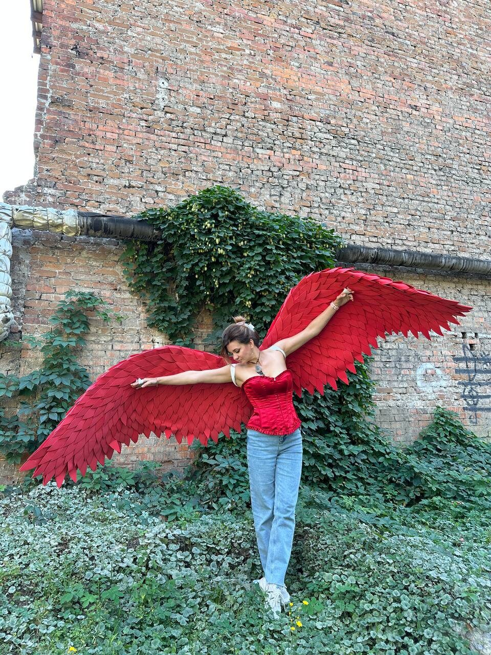 May include: A person wearing a red corset and blue jeans with large red feathered angel wings.