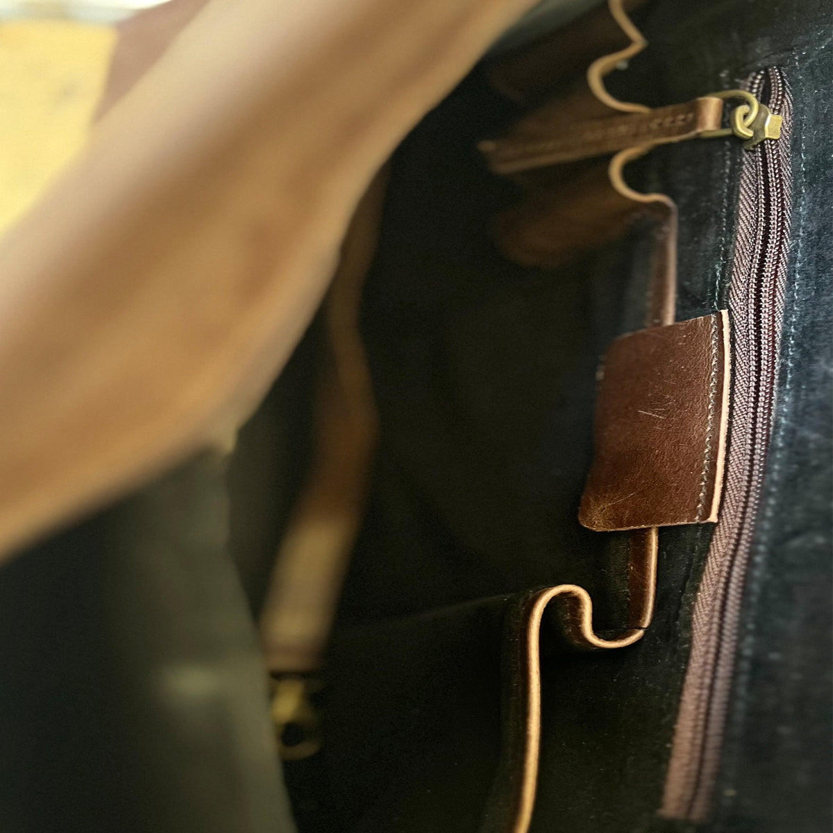 May include: Close-up of the inside of a brown leather bag with a zipper closure. The bag has a small, brown leather pocket on the inside.
