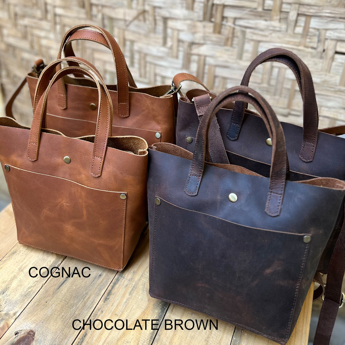 May include: Three leather tote bags in cognac, chocolate brown, and black. The bags have a single pocket on the front and a top handle.