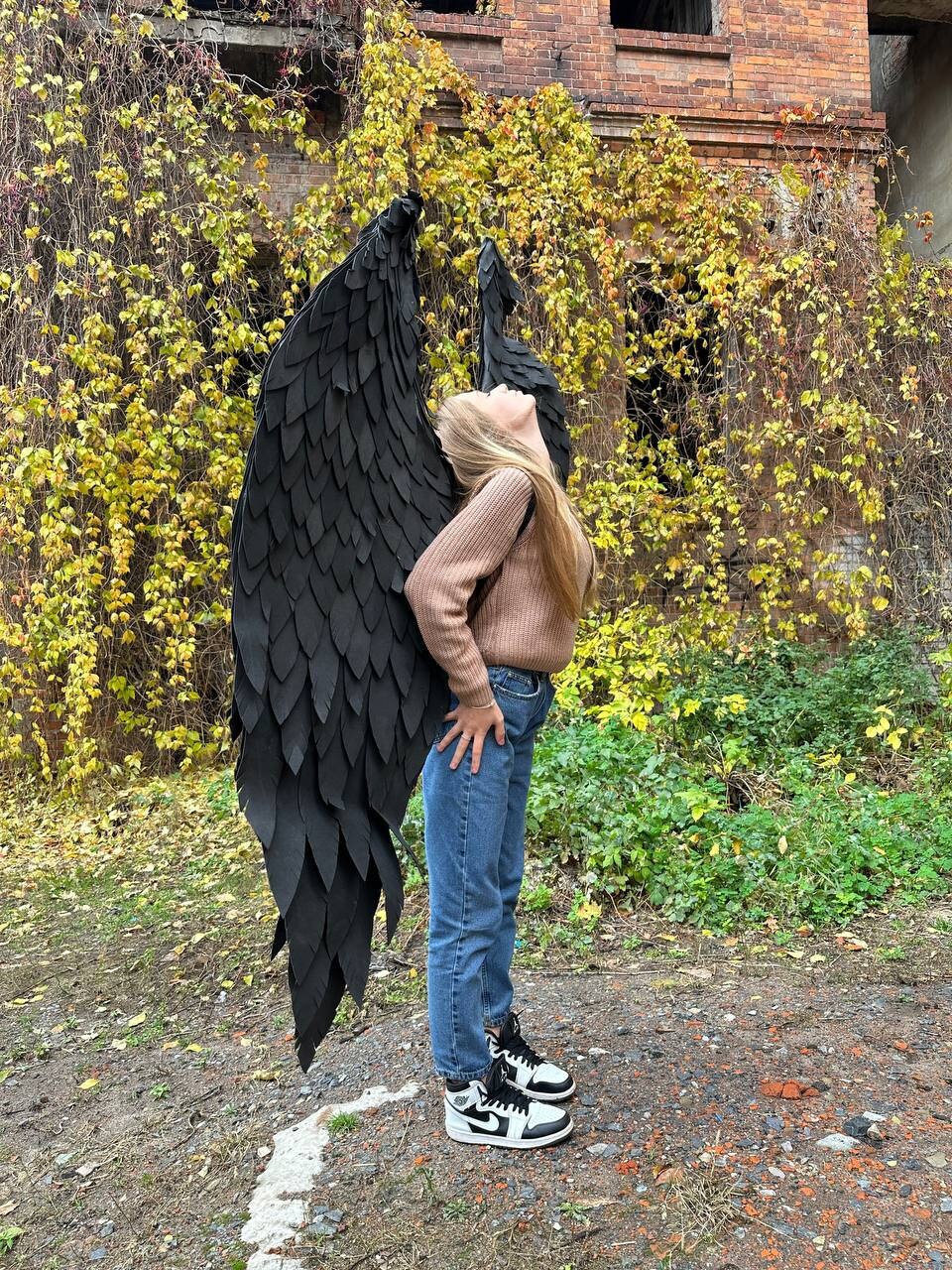 May include: A person wearing a brown sweater and blue jeans with black feathered angel wings.