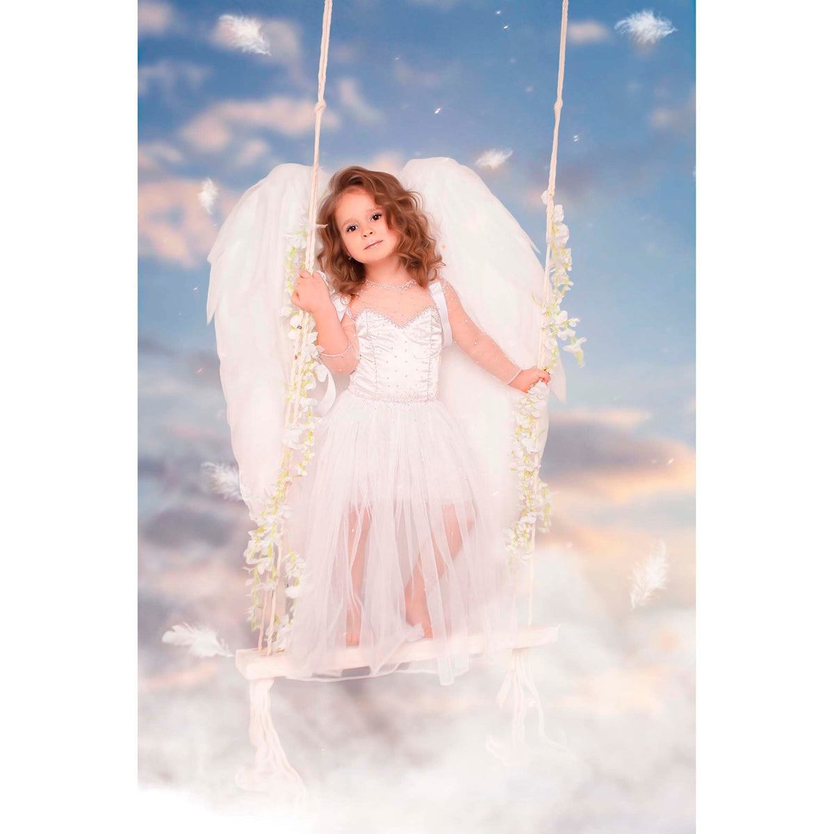 May include: A young girl dressed as an angel with white wings and a white dress is sitting on a swing. The swing is decorated with white flowers. The background is a blue sky with white clouds.