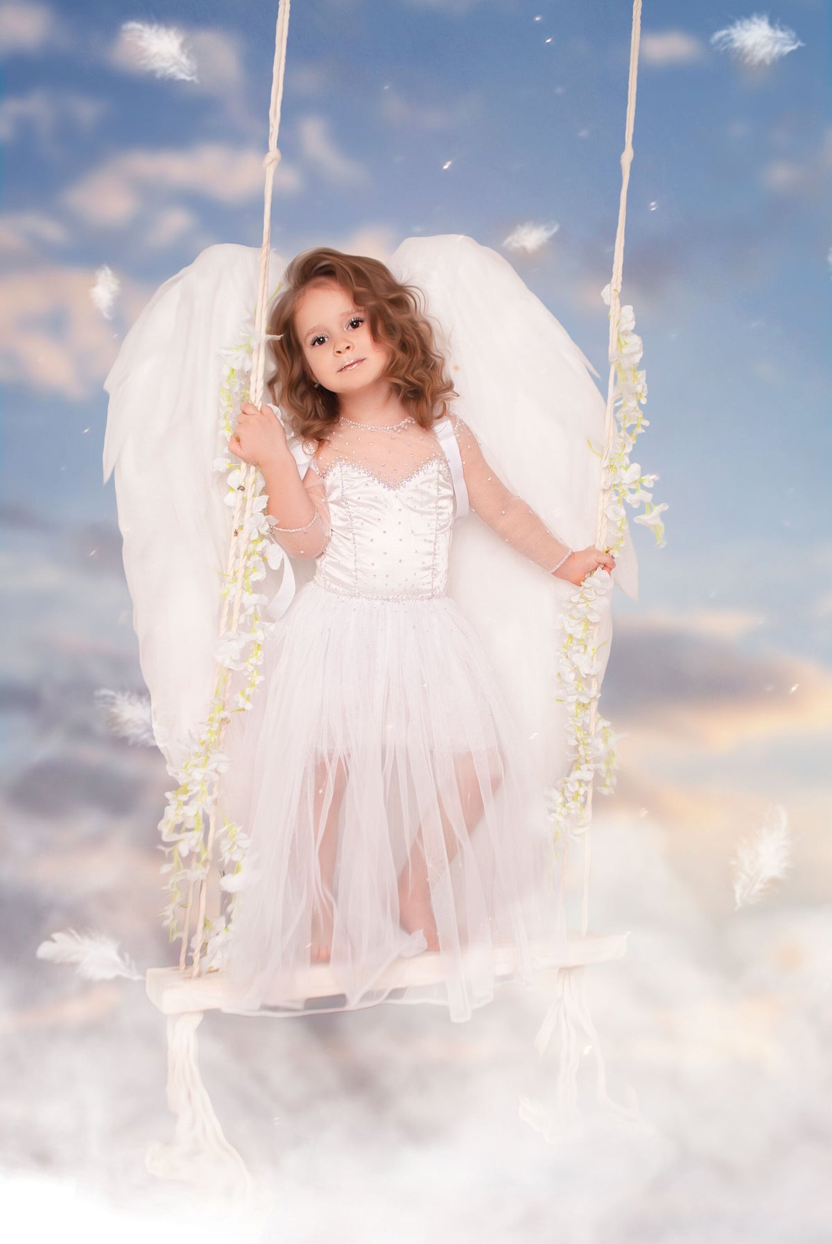 May include: A young girl dressed as an angel with white wings and a white dress sits on a swing against a blue sky with clouds.