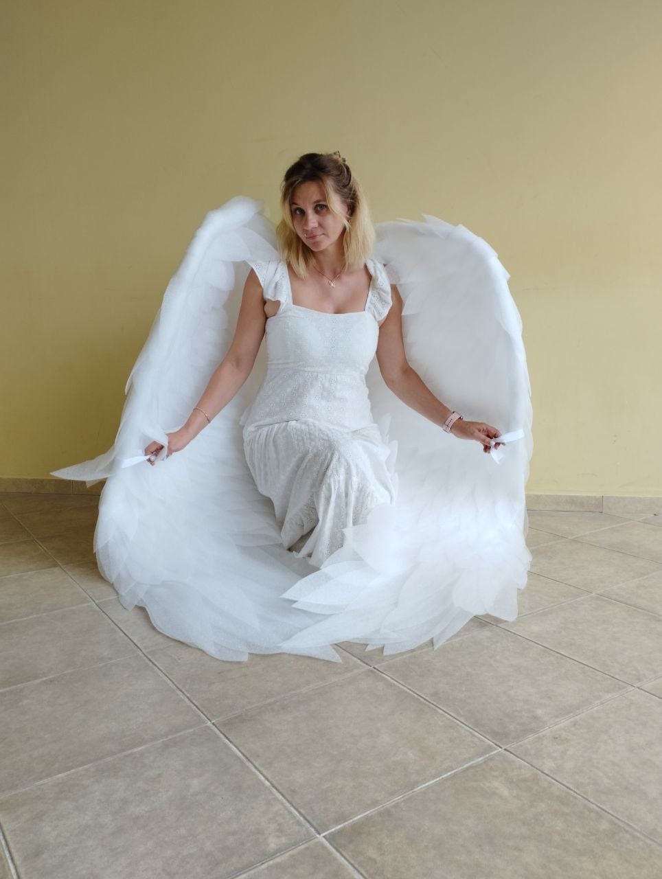 May include: A woman wearing a white dress and large white angel wings. The wings are made of soft, feathery material and are spread out behind her.