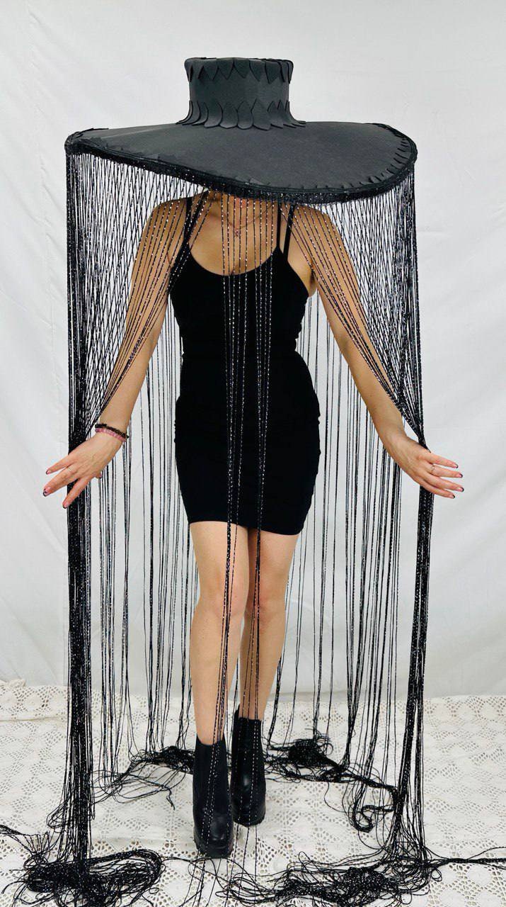 May include: A black wide-brimmed hat with a beaded fringe. The hat is worn by a person with a black dress and black boots.