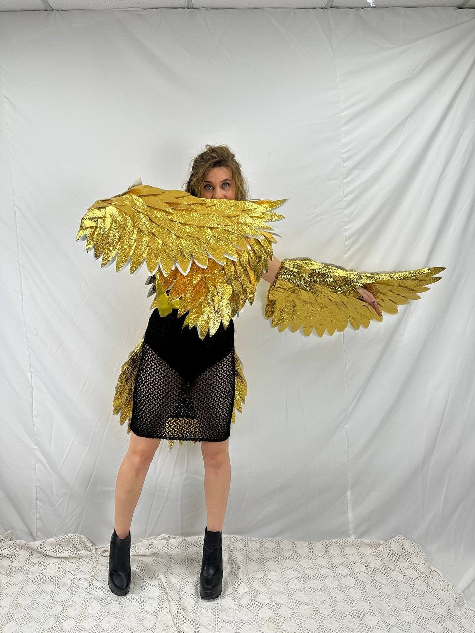 May include: A person wearing a gold costume with wings, a black mesh skirt, and black boots. The costume is made of feathers and is very detailed.