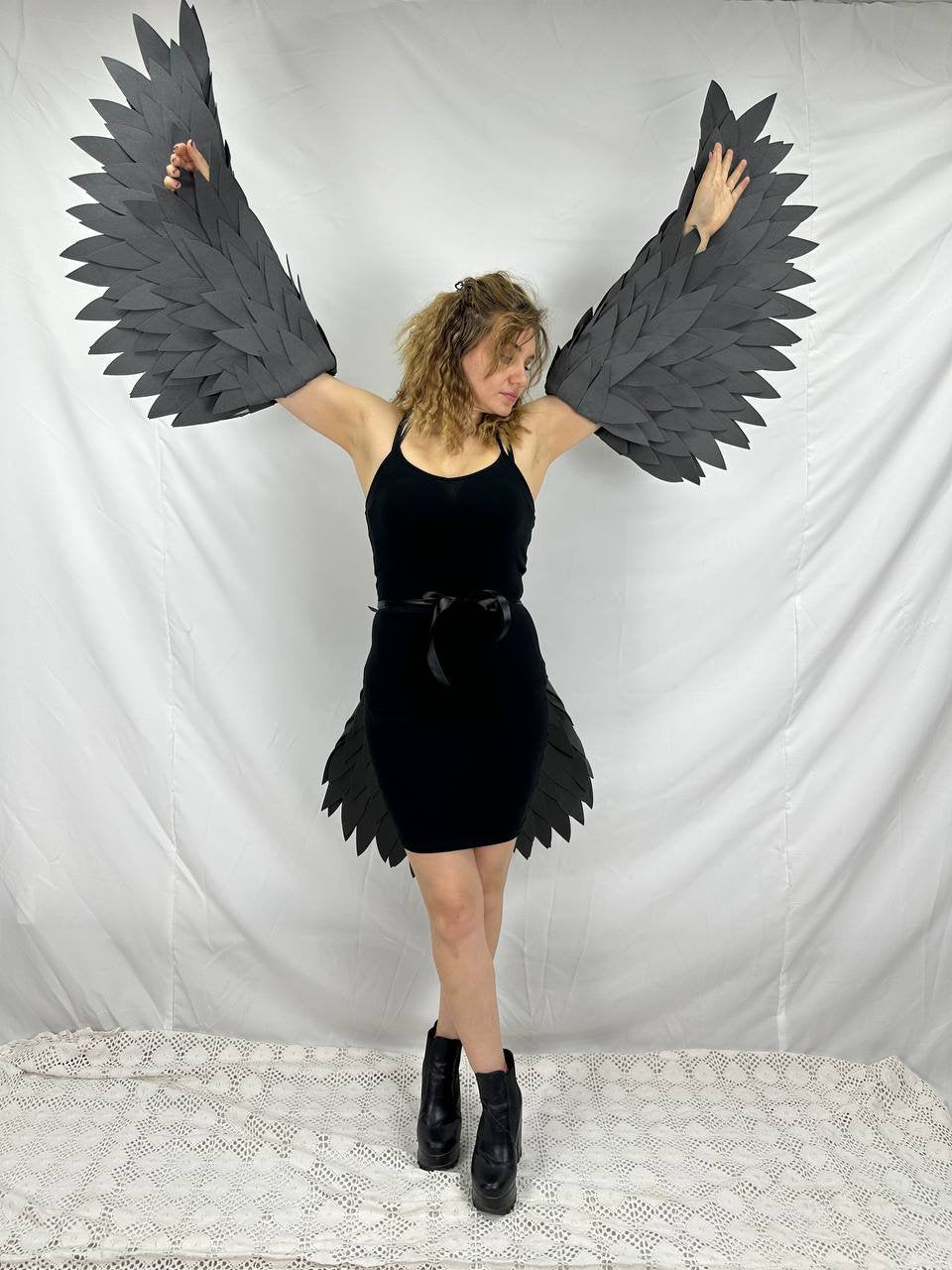 May include: A person wearing a black dress with black feathered wings attached to the arms and legs. The wings are made of paper and are spread out.