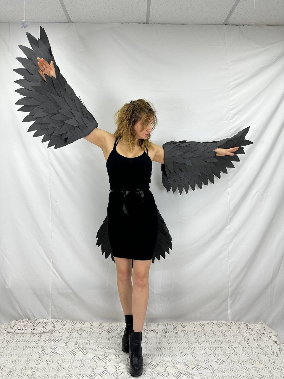 May include: A person wearing a black dress with black feathered wings attached to their arms.