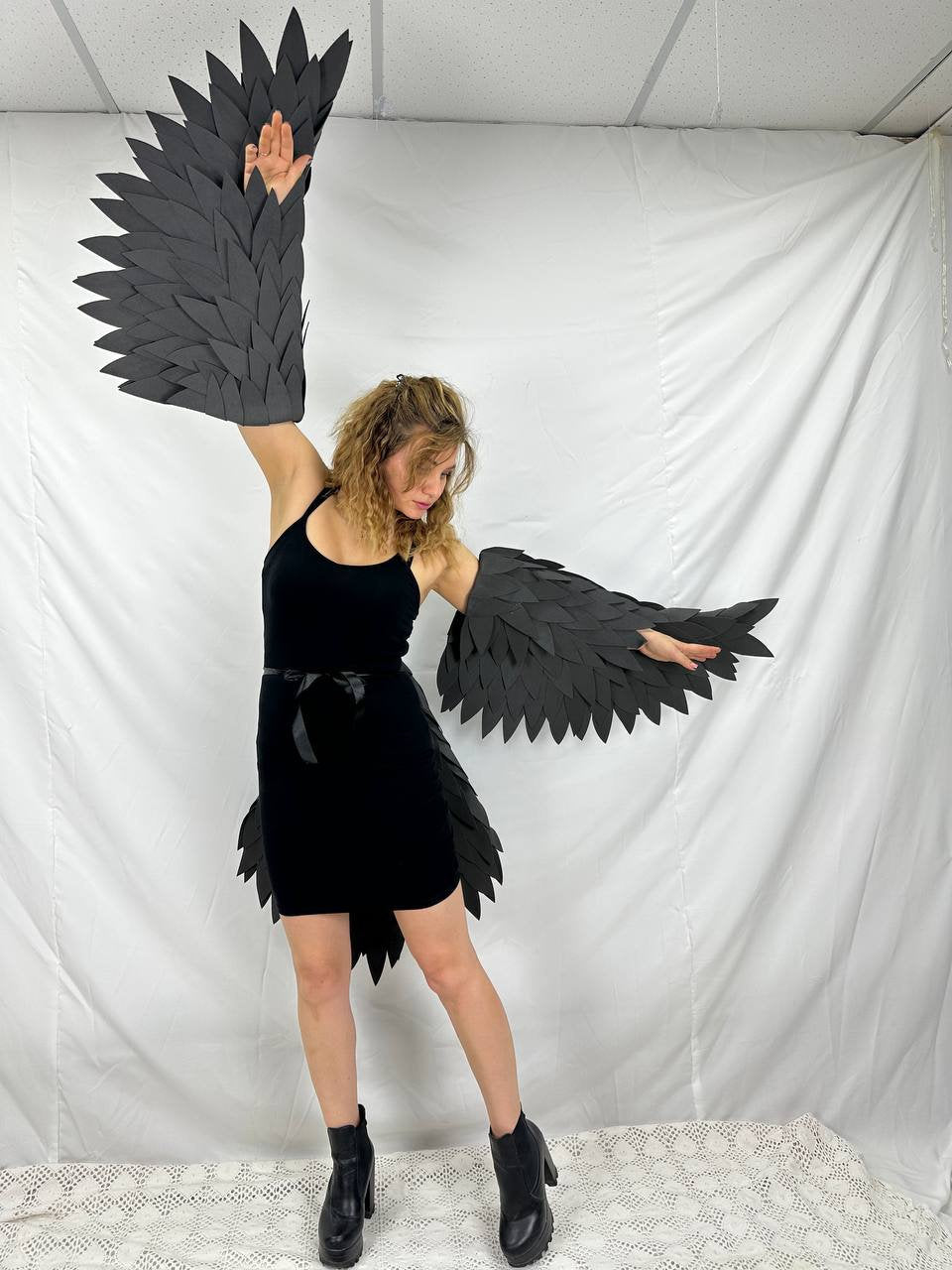 May include: A person wearing a black dress and black boots with large black feathered wings attached to their arms.
